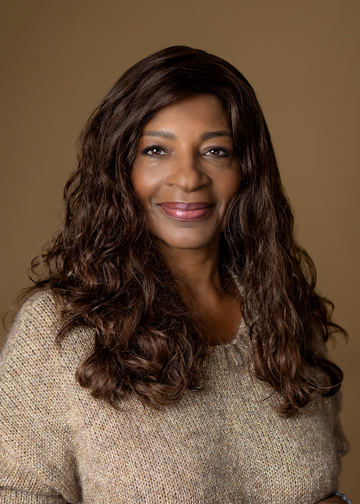 Smiling woman with long dark brown curly hair wearing a beige jumper