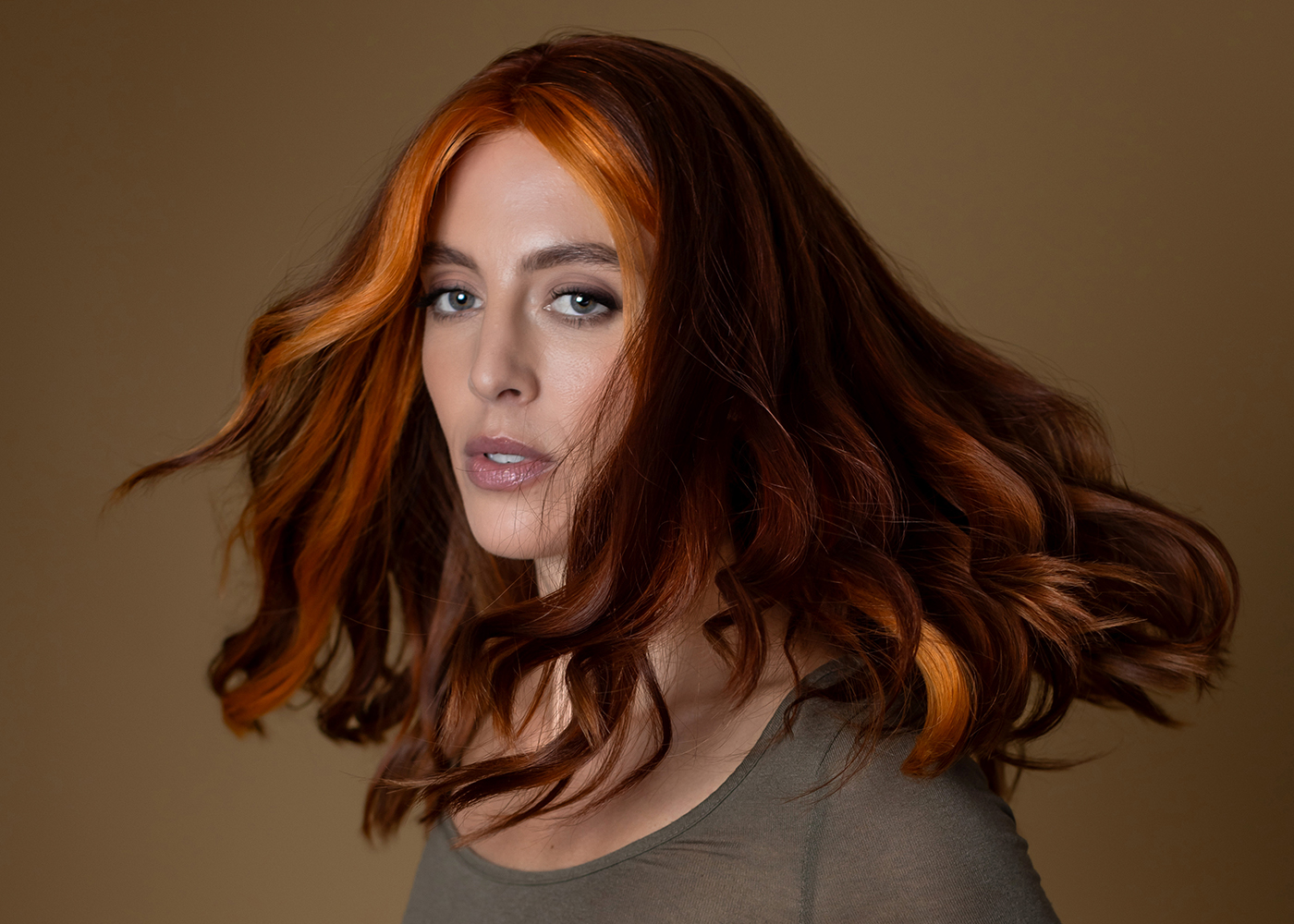 Woman with vibrant copper-red wavy hair posing against beige background.