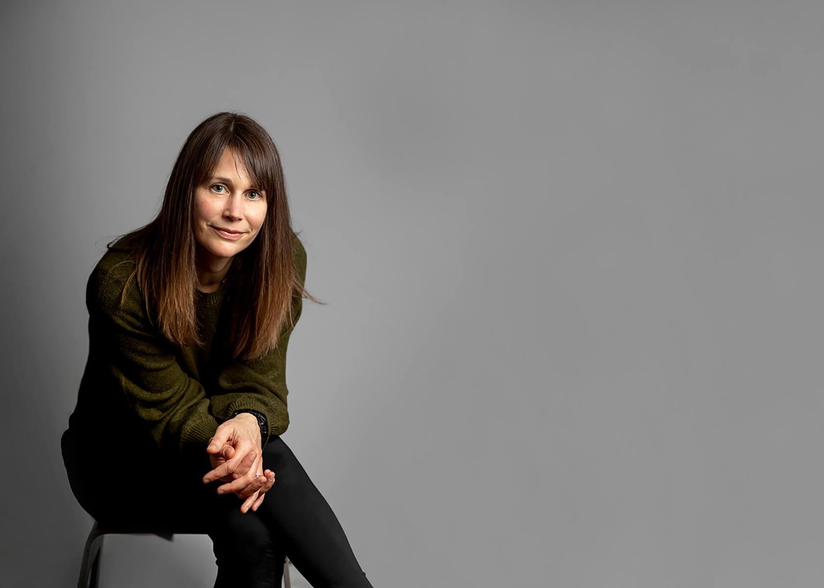Professional studio portrait of a woman seated against a grey background